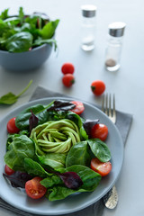 Salad mix with avocado, spinach, tomatoes and beet leaves on gray wooden background. Vegetarian food concept. Selective focus.