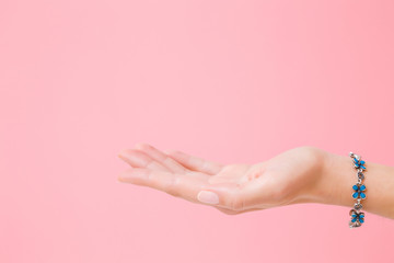 Hand holding nothing. Blue flower bracelet on woman's wrist. Isolated on pastel pink background. Closeup. Empty place for objects, business product or text. Side view. - obrazy, fototapety, plakaty