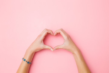 Heart shape created from young woman's hands on pastel pink background. Love and happiness concept....