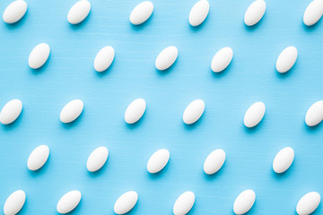 White pills on light pastel blue table. Drugs pattern. Medical, pharmacy and healthcare concept. Closeup. 