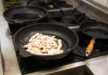 Slices of chicken fillet meat fried in a frying pan in the kitchen in the restaurant, close-up