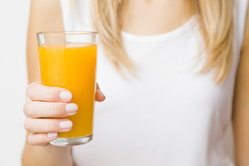 Young blonde woman in white shirt. Hand holding glass of orange juice. Tasty, healthy drink. Front view. Closeup.