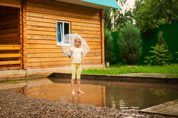 Blonde girl with umbrella jumping on the puddles