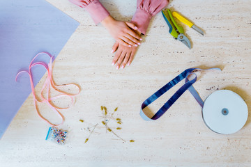 cropped view of female designer with ribbons, pins, wrapping paper and tools on table