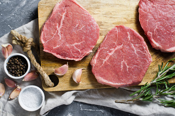 Beef steak tenderloin on a wooden chopping Board, garlic and a sprig of rosemary. Top view, grey background. - obrazy, fototapety, plakaty