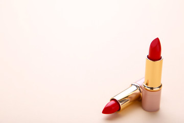 Two red lipsticks on beige background, close up