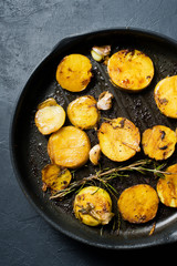 Traditional English fried potatoes with garlic and rosemary in a frying pan. Top view, black background.