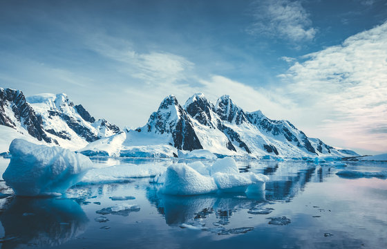 Blue Ice covered mountains in south polar ocean. Winter Antarctic landscape. The mount's reflection in the crystal clear water. The cloudy sky over the massive rock glacier. Travel wild nature