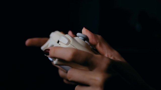 Young female gamer with gamepad or joystick playing video game in dark room. Gaming, fun, leisure time and entertainment concept