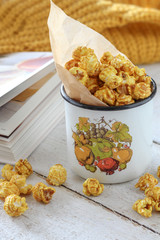 Golden color popcorn in mug and yellow sweater on a white wooden table 