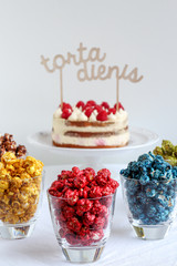 Party table with colorful popcorn in glasses and cake in the background