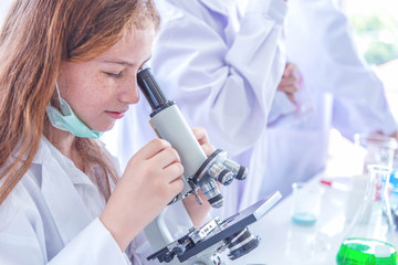 Little girl at an elementary school, using microscope research, testing in science class. Toddler girl doing biochemistry research in lab. Child have experiment with test tubes in bright modern lab.