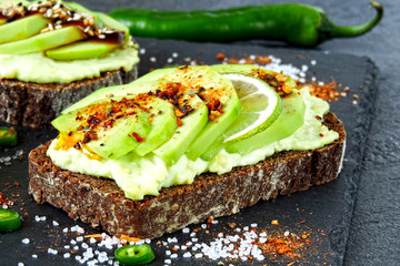 Beautifully plated avocado toast with delicious-looking toppings. Healthy Avocado Toasts on a Gray Stone Board.