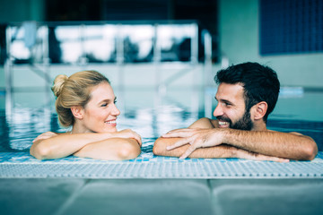 Happy attractive couple relaxing in swimming pool - obrazy, fototapety, plakaty
