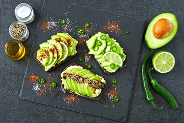 Healthy avocado toasts with spices, lime and chili, presented on a gray stone board.