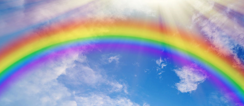 Colorful rainbow and sun rays on blue cloudy sky
