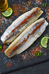 Herring fillet with sea salt and spices on a gray stone board.