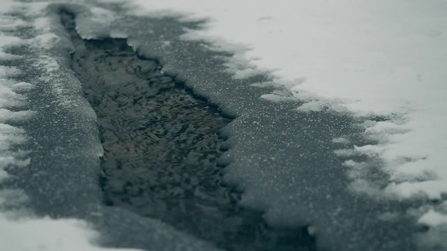 Thawed patch on frozen river. Frozen ice river is melting in spring with ice flakes flowing. Cracked ice floating on the river in spring time. Global warming