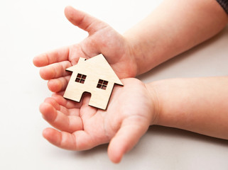 A little child holds wooden flat house in his hands on the white background