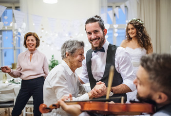 A young groom dancing with grandmother on a wedding reception.