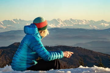 Junge Frau sitzt auf einem Berg und betrachtet das Alpenpanorama