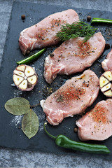 Raw pork steaks with spices before cooking. Appetizing meat on a stone board with spices. The recipe for pork steaks. Raw pork steaks are marinated in seasonings.