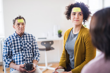 Men and women sitting in a circle during group therapy, adhesive notes on forehead.