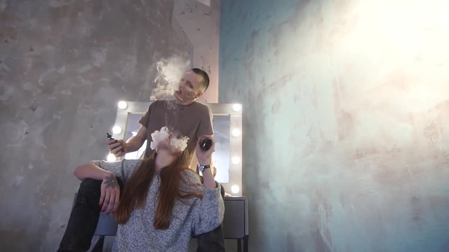 A loving couple on a bed smokes electronic cigarettes.