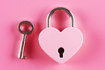 The concept of finding love. The lock in the shape of a heart and the key to it on a pink background