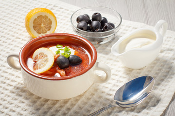 Soup saltwort with meat, potatoes, tomatoes, lemon, black olives and sour cream in ceramic soup bowl.