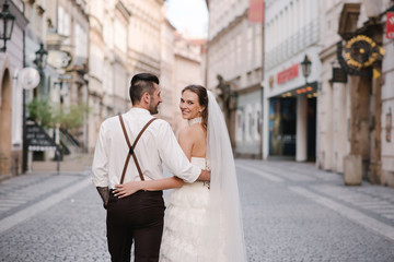 Rear view of happy wedding couple walking on the beautiful old streets of Prague city. Czech Republic