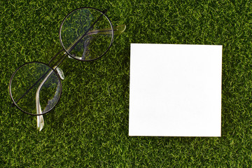 White stick note and glasses on a background of green grass. A place to write ideas and thoughts.