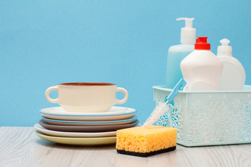 Bottles of dishwashing liquid in basket and plates on blue background.
