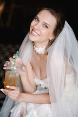 Young beautiful bride in white wedding dress sitting and drinking juice. Smiling bride before the ceremony
