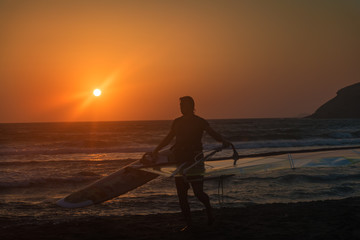 Windsurfer with his surf getting out of water on Prasonisi beach, sunset (Rhodes, Greece)