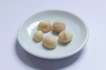 Top view of macadamia nuts in bowl on white background.