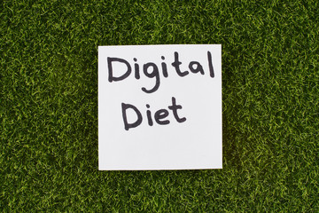 Inscription Digital Diet on a white sticker on the background of green grass. Gadgets detox concept.