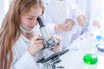 Little girl at an elementary school, using microscope research, testing in science class. Toddler girl doing biochemistry research in lab. Child have experiment with test tubes in bright modern lab.