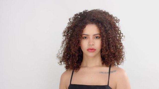 mixed race black woman with freckles and curly hair in studio on white poses to a camera touches her big hair and watching aside