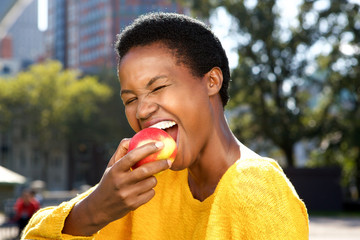 Close up healthy young black woman eating apple outdoors