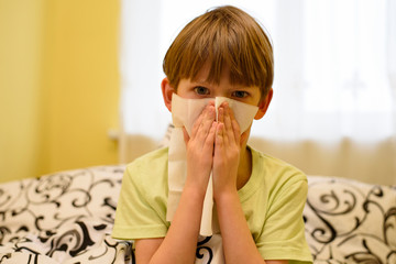 Sick boy blow his nose into tissue in bedroom.