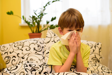 Sick kid blowing nose into tissue. Running nose or sneezing and covering his nose. Allergic Rhinitis.