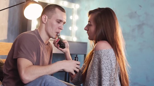A loving couple on a bed smokes electronic cigarettes.
