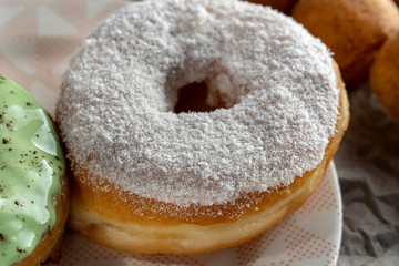Two donuts, one with icing, the second is sprinkled with coconut chips.