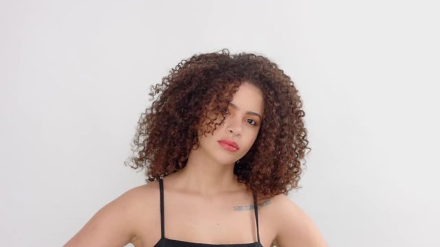 mixed race black woman with freckles and curly hair in studio on white poses to a camera looks serious