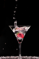 Cocktail with strawberries isolated on black background.Glass of vodka splashing.