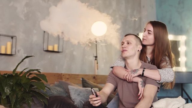 A loving couple on a bed smokes electronic cigarettes.