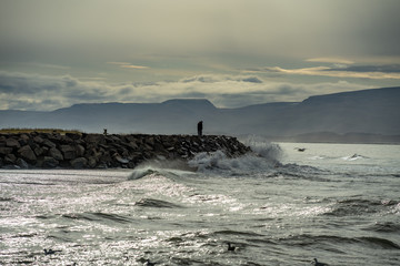 People watching the waves rolling in at a pier in northern Iceland