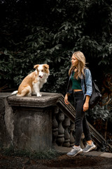 cute sexy blonde Girl in cool jeans jacket in park with her dog, border collie