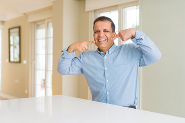 Fototapeta premium Middle age man sitting at home smiling confident showing and pointing with fingers teeth and mouth. Health concept.